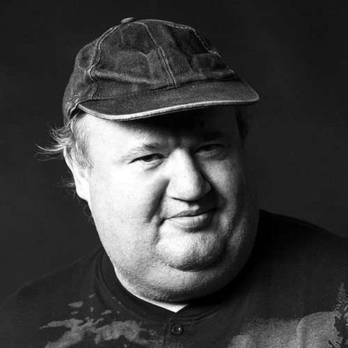 Hans Dröbl, VOI fesch Künstler; ein schwarz-weiß Foto, er trägt eine Kappe, an den Schläfen sind Haare sichtbar, er lächelt leicht und blickt in die Kamera