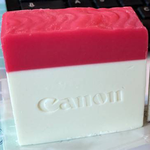 Canon Seife von HautSinn; die Seife ist zu etwa einem Drittel rot (oben) und der untere Teil zwei Drittel in weißer Farbe, im weißen Teil der Seife ist das Wort Canon eingestempelt