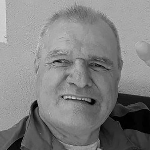 Gottfried Varecka, VOI fesch Künstler; auf dem schwarz-weiß Foto sind seine kurzen, eher grauen Haare zu sehen, sein Kopf schaut Richtung Kamera, mit seinen Augen schaut er etwas zur Seite, er lächelt und dabei werden seine Zähne sichtbar