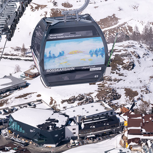im Bild ist die fahrende Gondel von Sponsor*in Gurgl Carat zu sehen, darunter eine Winterlandschaft mit Schnee, das Gurgl Carat Gebäude ist auch sichtbar