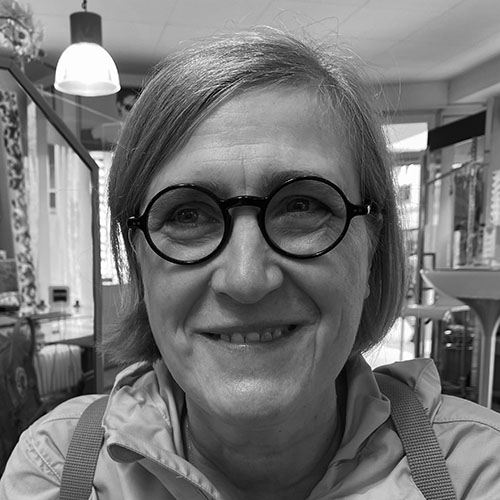Sabine Tollkühn-Klein, VOI fesch Künstlerin; ein schwarz-weiß Foto zeigt sie mit kinnlangen Haaren, seitlich hinter die Ohren gelegt, sie trägt eine runde, schwarze Brille und lächelt in die Kamera, leicht werden ihre Zähne dabei sichtbar