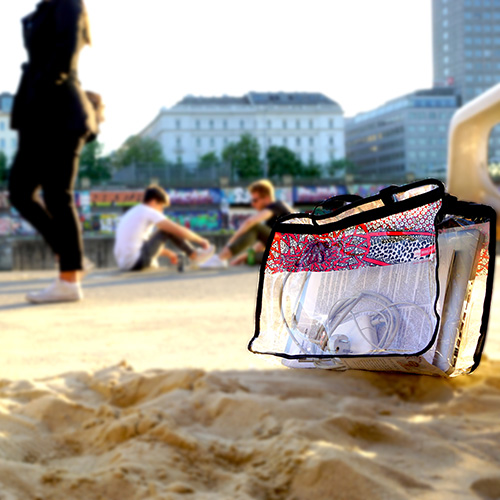 BIBLIOBAGS Tasche mit VOI fesch Design von Künstlerin Patricia Hütter, vorne im Bild und auf Sanduntergrund; im Hintergrund sind Menschen am Wiener Donaukanal zu sehen